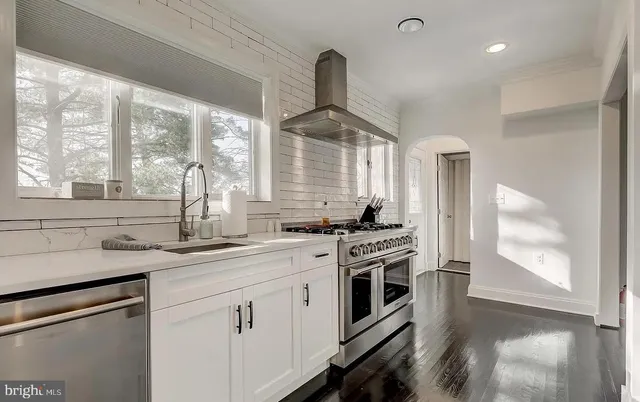 a kitchen with stainless steel appliances granite countertop a refrigerator a sink dishwasher a stove and white cabinets with wooden floor