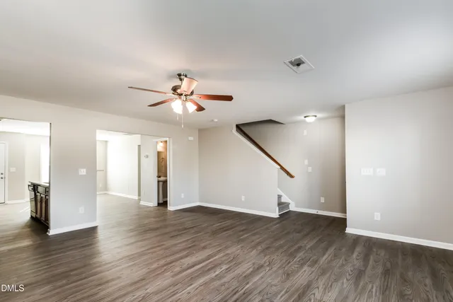 a view of an empty room with wooden floor and a ceiling fan