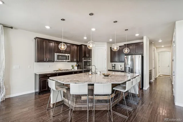 a kitchen with stainless steel appliances kitchen island granite countertop a dining table chairs and wooden floor