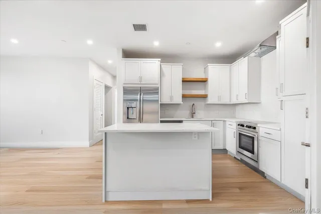 a kitchen with stainless steel appliances granite countertop a stove top oven a sink dishwasher and a refrigerator with wooden floor