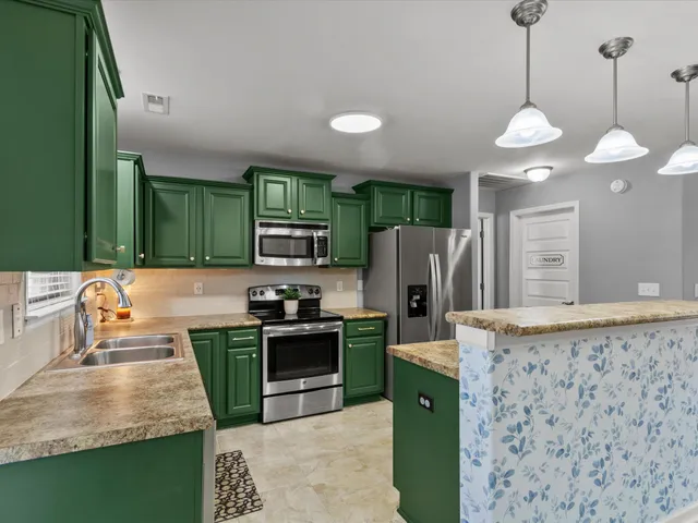 a kitchen with stainless steel appliances granite countertop a sink a stove a refrigerator a washer dryer and a dining table