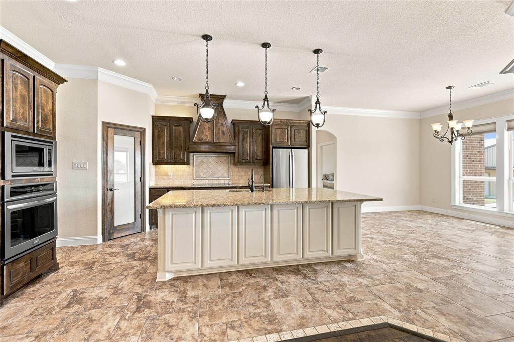 420 Hartley Way Azle, TX 76020 - Photo 10 of 40 Spacious kitchen featuring an island with stone countertops, built-in ovens and microwave, dark wood-finish cabinetry, and tile flooring