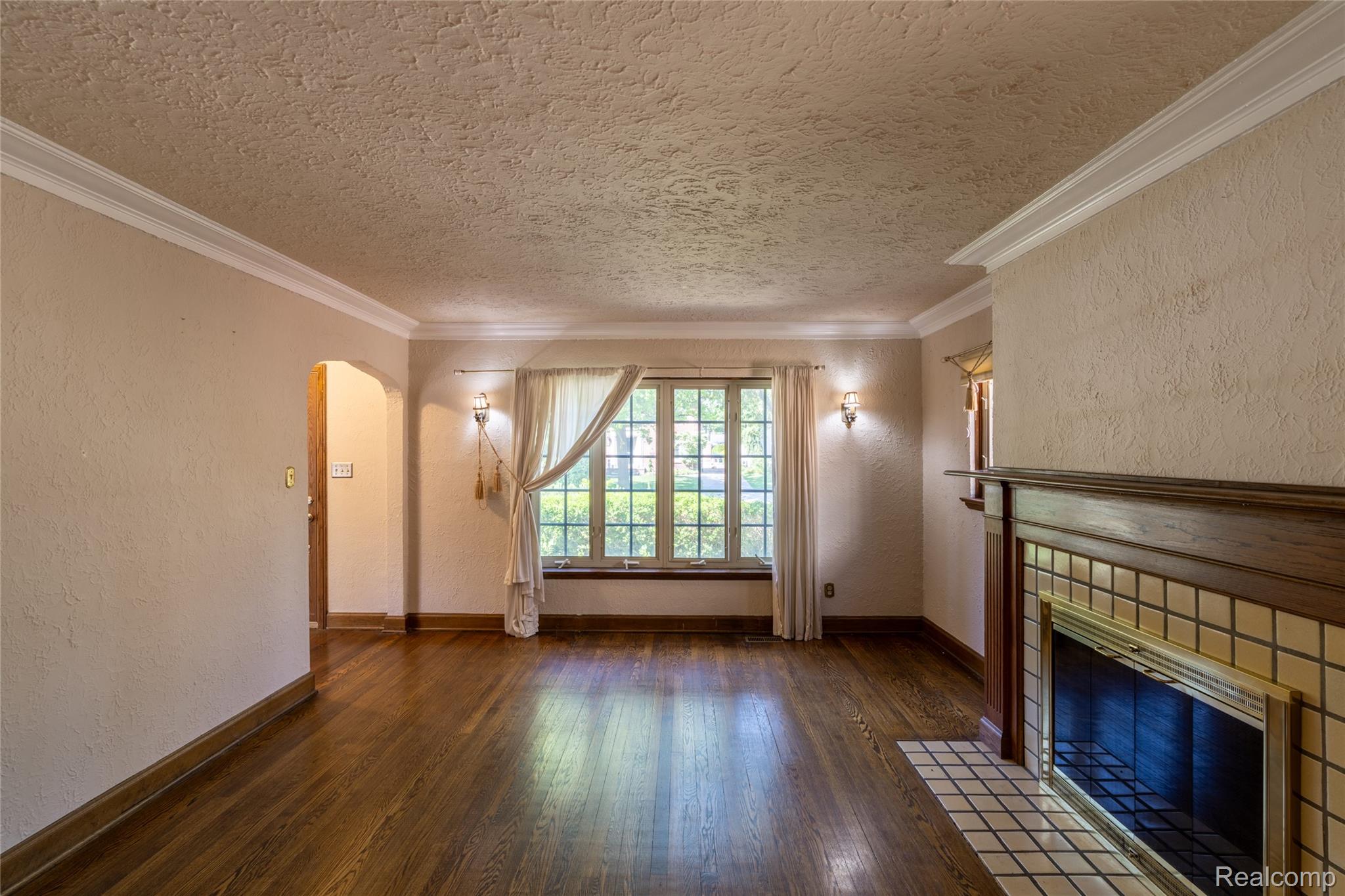 1481 Oxford Road Grosse Pointe, MI 48236 - Photo 29 of 29 Living space featuring a wood-finish floor, detailed fireplace with tile surround, arched doorway, and built-in wall sconces