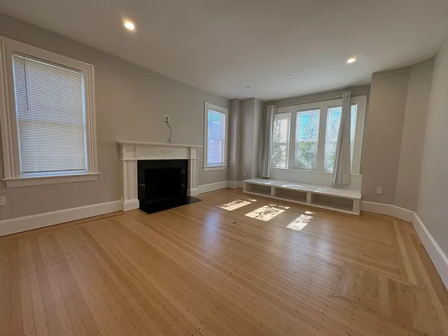 an empty room with wooden floor fireplace and windows