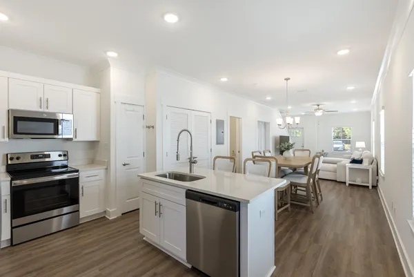 a open kitchen with stainless steel appliances kitchen island granite countertop a stove a sink a refrigerator and white cabinets with wooden floor