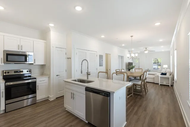 a open kitchen with stainless steel appliances kitchen island granite countertop a stove a sink a refrigerator and white cabinets with wooden floor