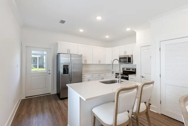 a kitchen that has a refrigerator a stove top oven a sink dishwasher and white cabinets with wooden floor