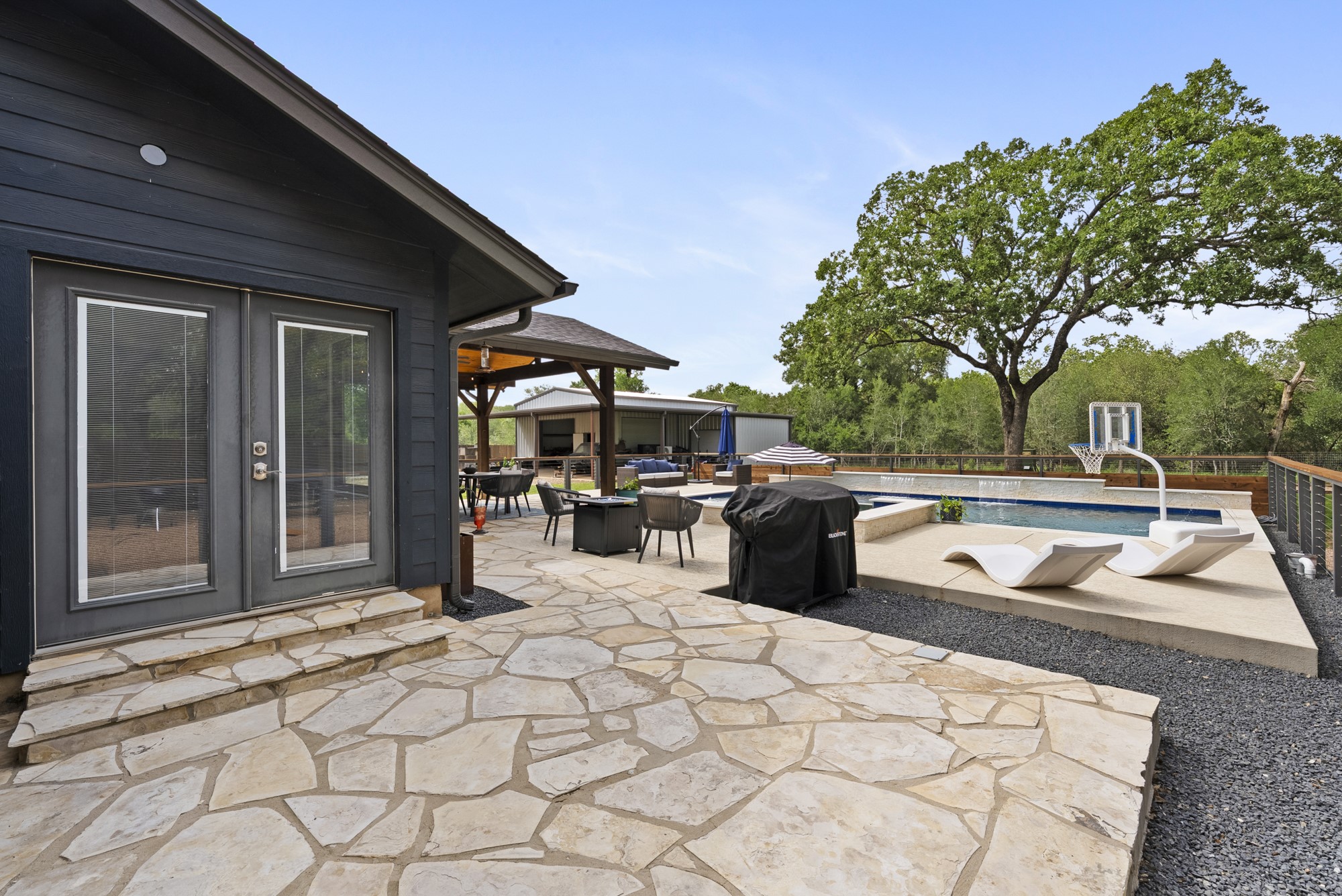 2802 Robin Road Manchaca, TX 78652 - Photo 17 of 40 Rear exterior with a freeform stone patio, dual glass doors, and a swimming pool