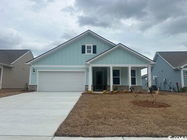 View of front of property with board and batten siding, brick siding, a garage, driveway, and a yard
