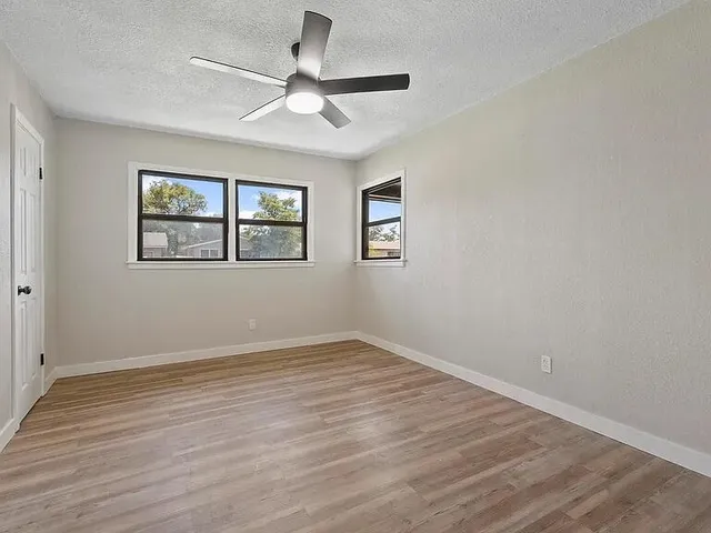 an empty room with wooden floor ceiling fan and windows