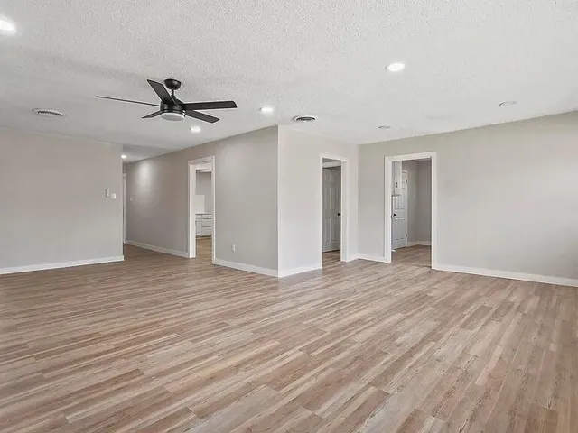 a view of an empty room with wooden floor and a ceiling fan