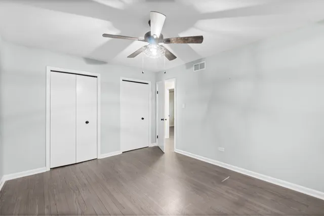 an empty room with wooden floor fan and windows