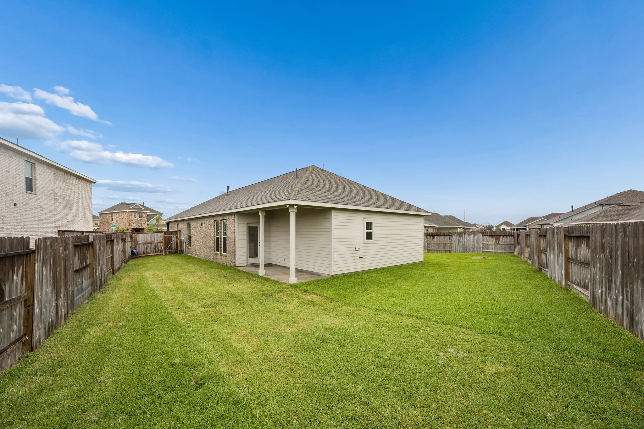 10902 Bonfire Trail Beasley, TX 77417 - Photo 27 of 36 This photo showcases a well-maintained backyard with a spacious lawn and a wooden fence. The house features a brick exterior with a covered patio, ideal for outdoor relaxation.