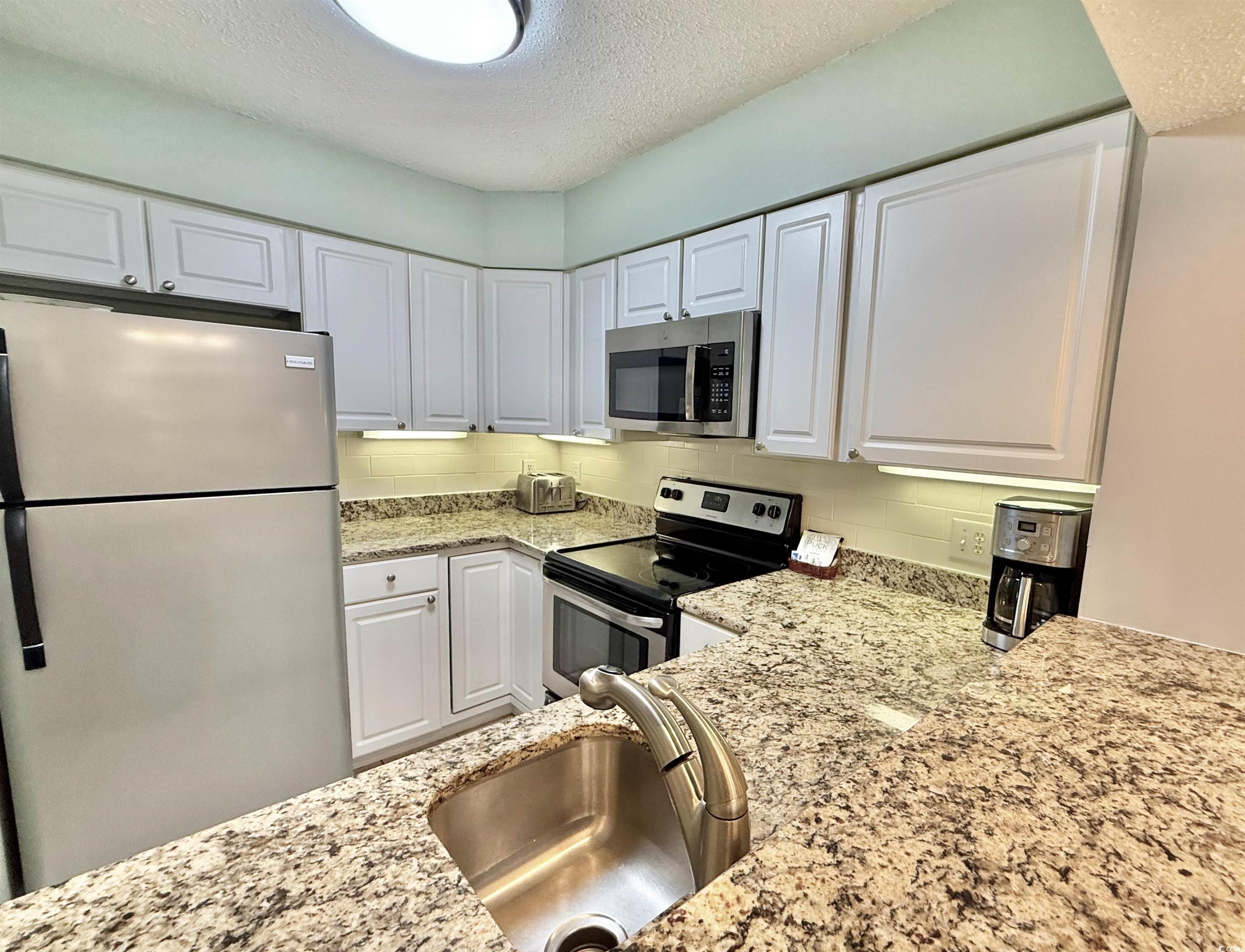 410 Melrose Place, Unit 310 Myrtle Beach, SC 29572 - Photo 15 of 39 Kitchen featuring stainless steel appliances, white cabinets, light stone countertops, a textured ceiling, and backsplash