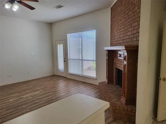 an empty room with wooden floor kitchen view and windows