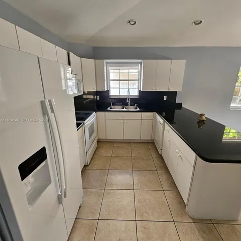 a large white kitchen with a sink a refrigerator and window