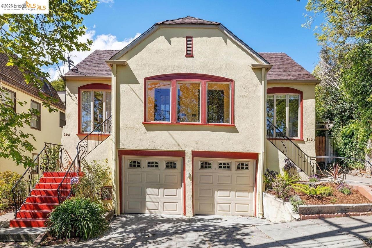 Stucco exterior with a pitched roof, featuring two garage doors, red-framed windows, and two external staircases with wrought iron railings
