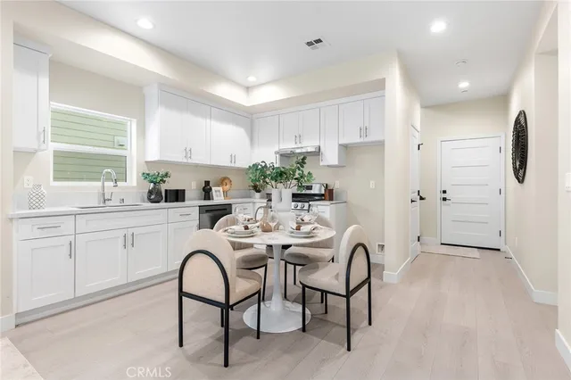 a kitchen with stainless steel appliances a dining table chairs a sink and white cabinets