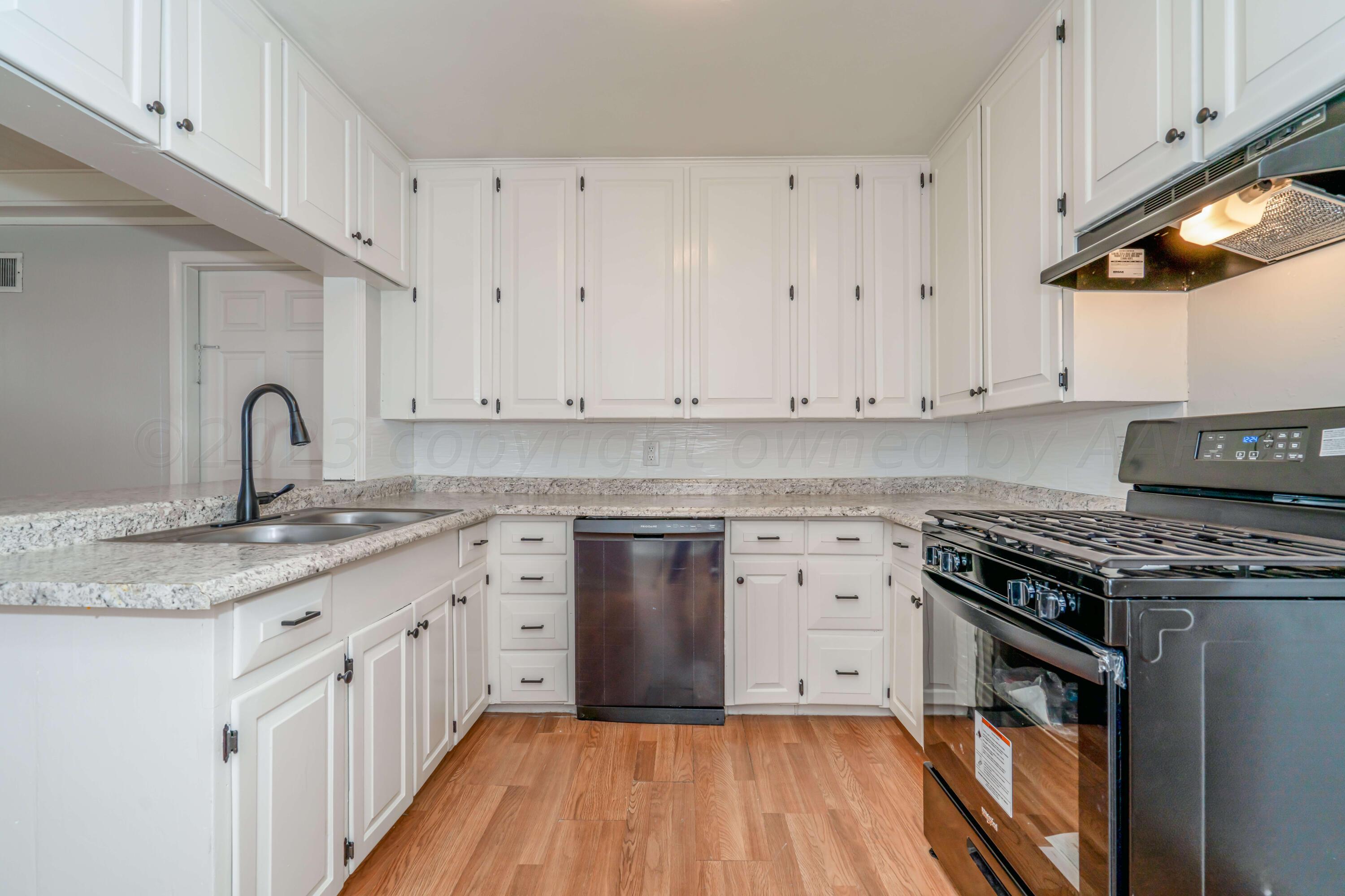 4306 Parker Street Amarillo, TX 79110 - Photo 8 of 29 a kitchen with granite countertop a stove top oven a sink dishwasher and white cabinets with wooden floor