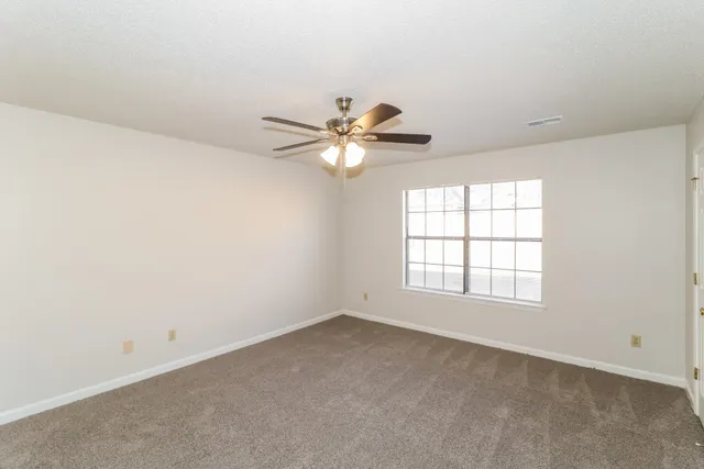an empty room with chandelier fan and windows