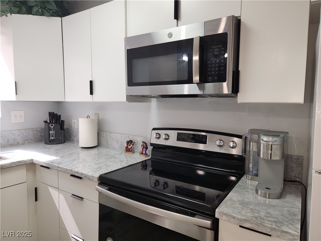 5045 Spencer Street, Unit B Las Vegas, NV 89119 - Photo 6 of 23 Kitchen with appliances with stainless steel finishes, white cabinetry, and light stone counters