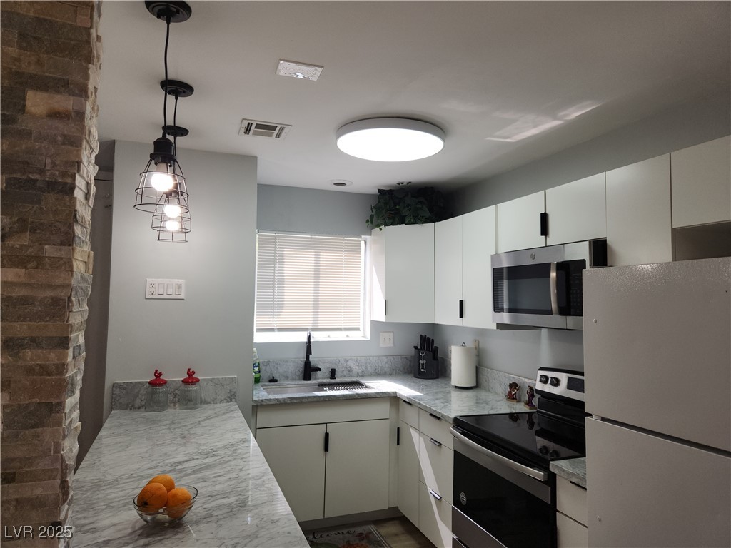 5045 Spencer Street, Unit B Las Vegas, NV 89119 - Photo 8 of 23 Kitchen featuring stainless steel appliances, light countertops, hanging light fixtures, and white cabinetry