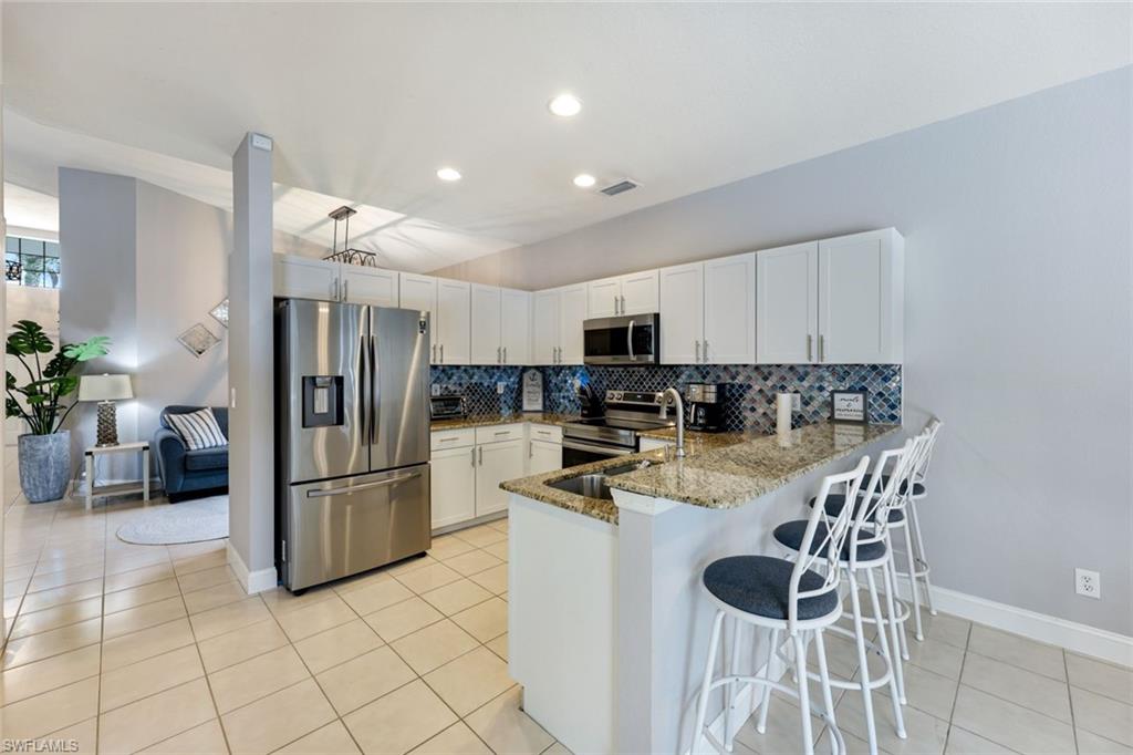 697 Crossfield Circle Naples, FL 34104 - Photo 6 of 18 Kitchen featuring stainless steel appliances, a peninsula, tasteful backsplash, stone countertops, and light tile patterned floors