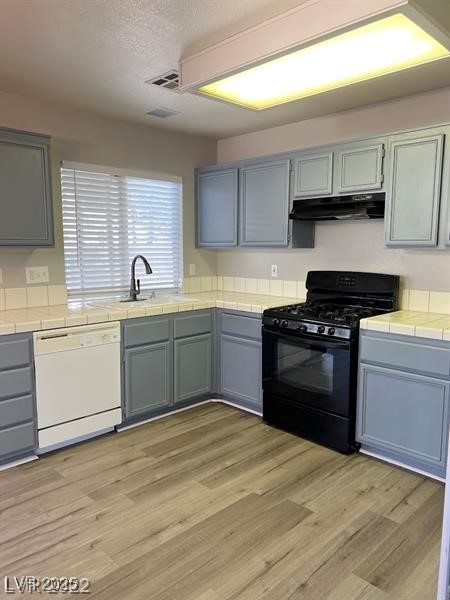 6532 Moon Roses Court Las Vegas, NV 89108 - Photo 4 of 8 Kitchen with tile counters, under cabinet range hood, gas stove, a sink, and dishwasher