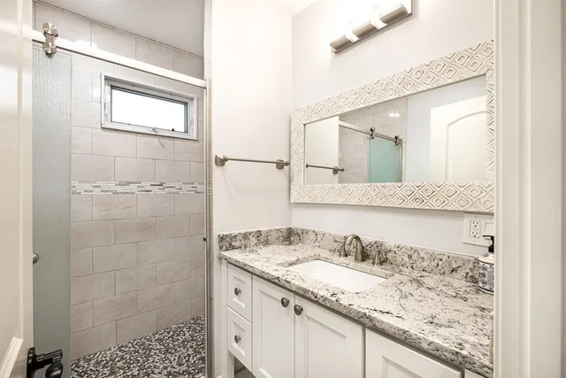 a bathroom with a granite countertop sink a mirror and a shower