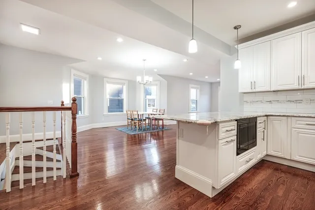 a kitchen with stainless steel appliances granite countertop a stove top oven a sink a dining table and chairs with wooden floor