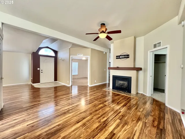 a view of a livingroom with a fireplace a ceiling fan and wooden floor