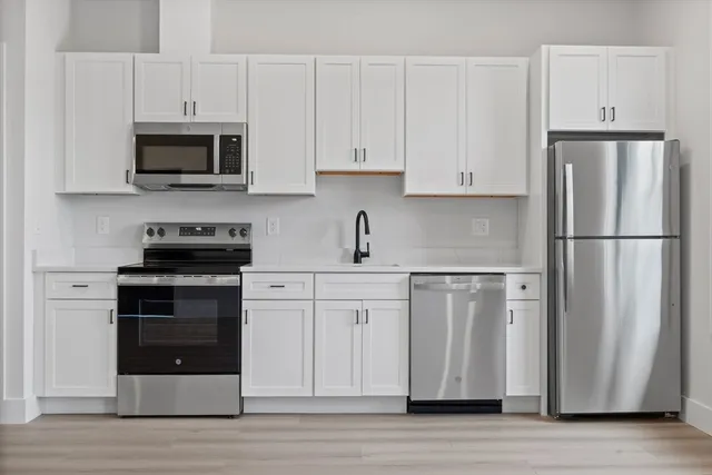 a kitchen with stainless steel appliances granite countertop a refrigerator stove a sink and white cabinets