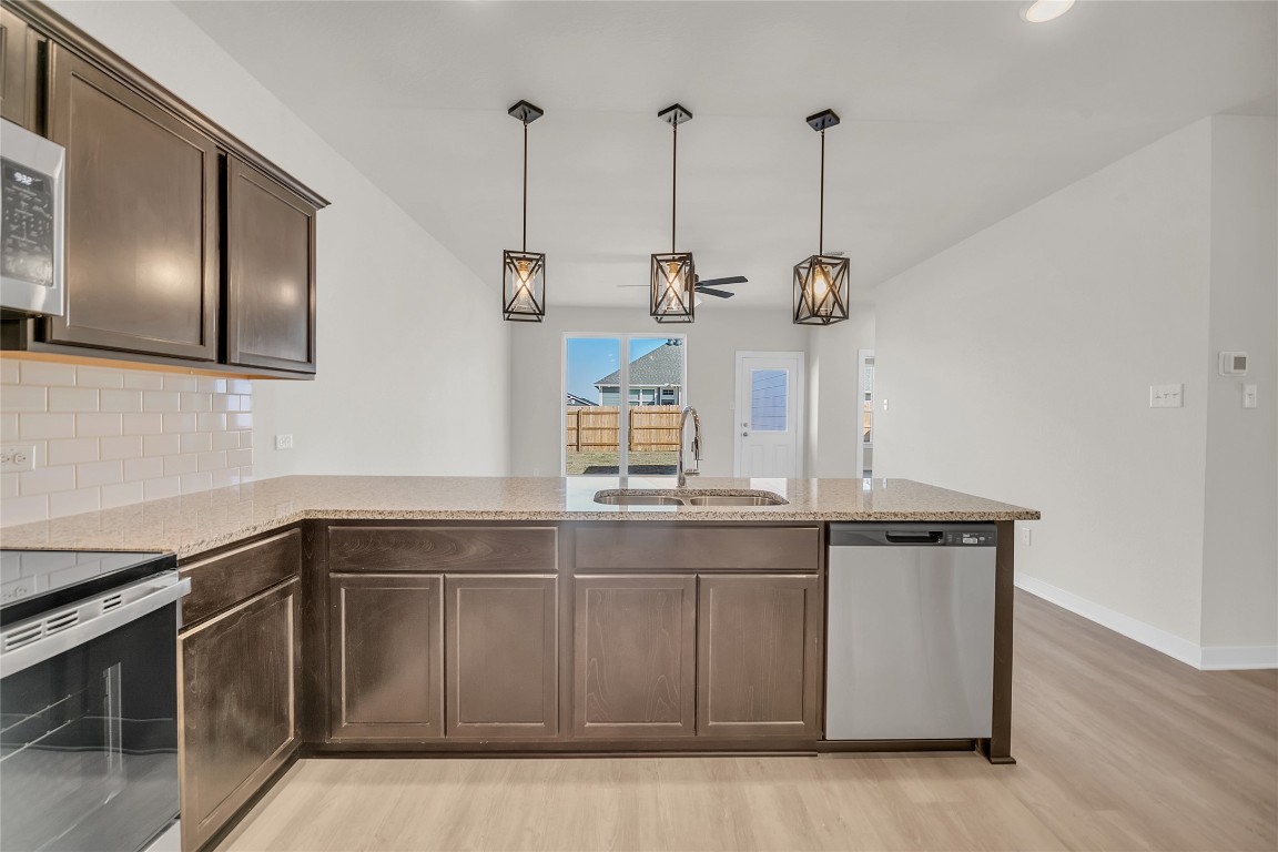 121 Walk Way Jarrell, TX 76537 - Photo 22 of 29 Kitchen featuring light stone countertops, a sink, stainless steel appliances, dark brown cabinetry, and backsplash