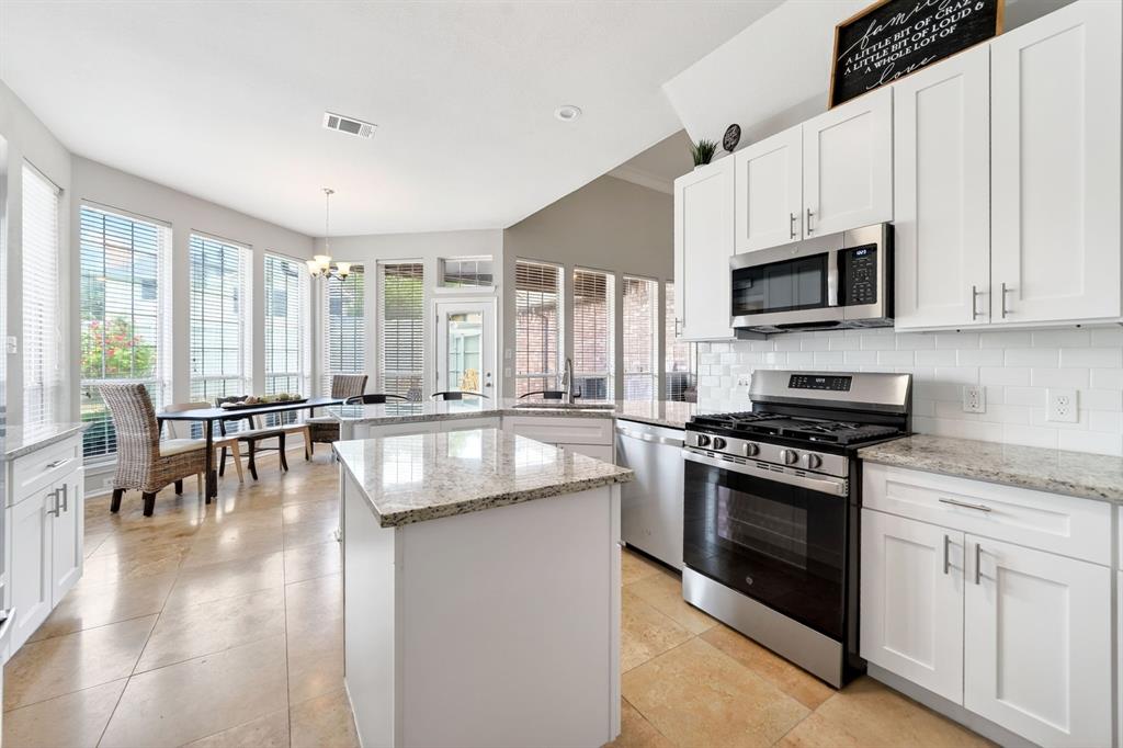 4509 Scenic Drive Rowlett, TX 75088 - Photo 16 of 40 Modern kitchen featuring white shaker cabinetry, stainless steel appliances, a center island with a stone-finish countertop, subway tile backsplash, and light-toned tile flooring