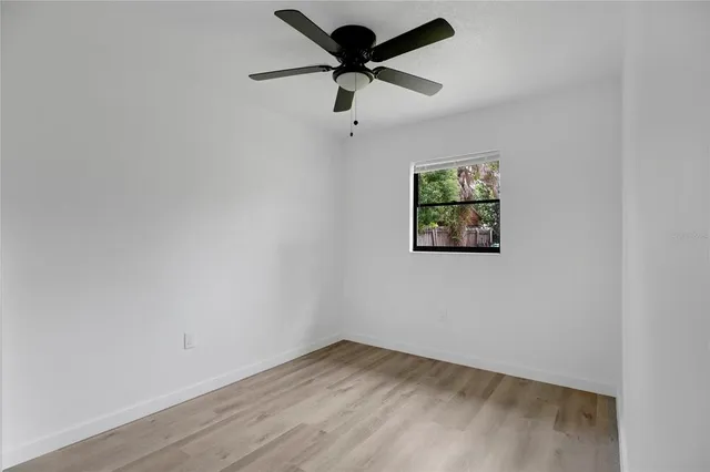an empty room with wooden floor fan and windows