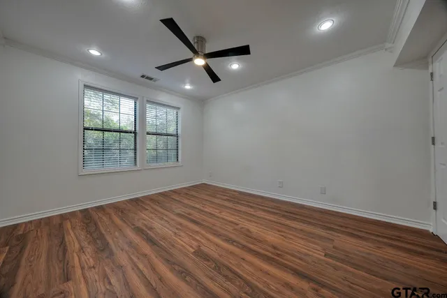 an empty room with wooden floor a ceiling fan and windows