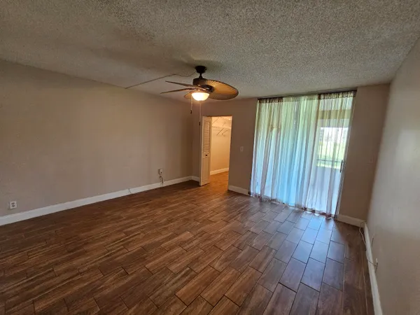 a view of an empty room with wooden floor and fan