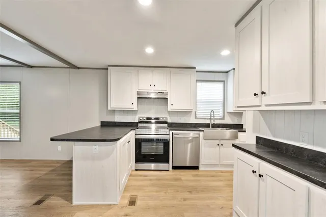 a kitchen with stainless steel appliances granite countertop a stove a sink and white cabinets