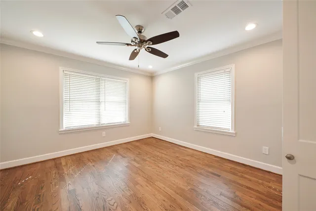 a view of an empty room with wooden floor and a ceiling fan
