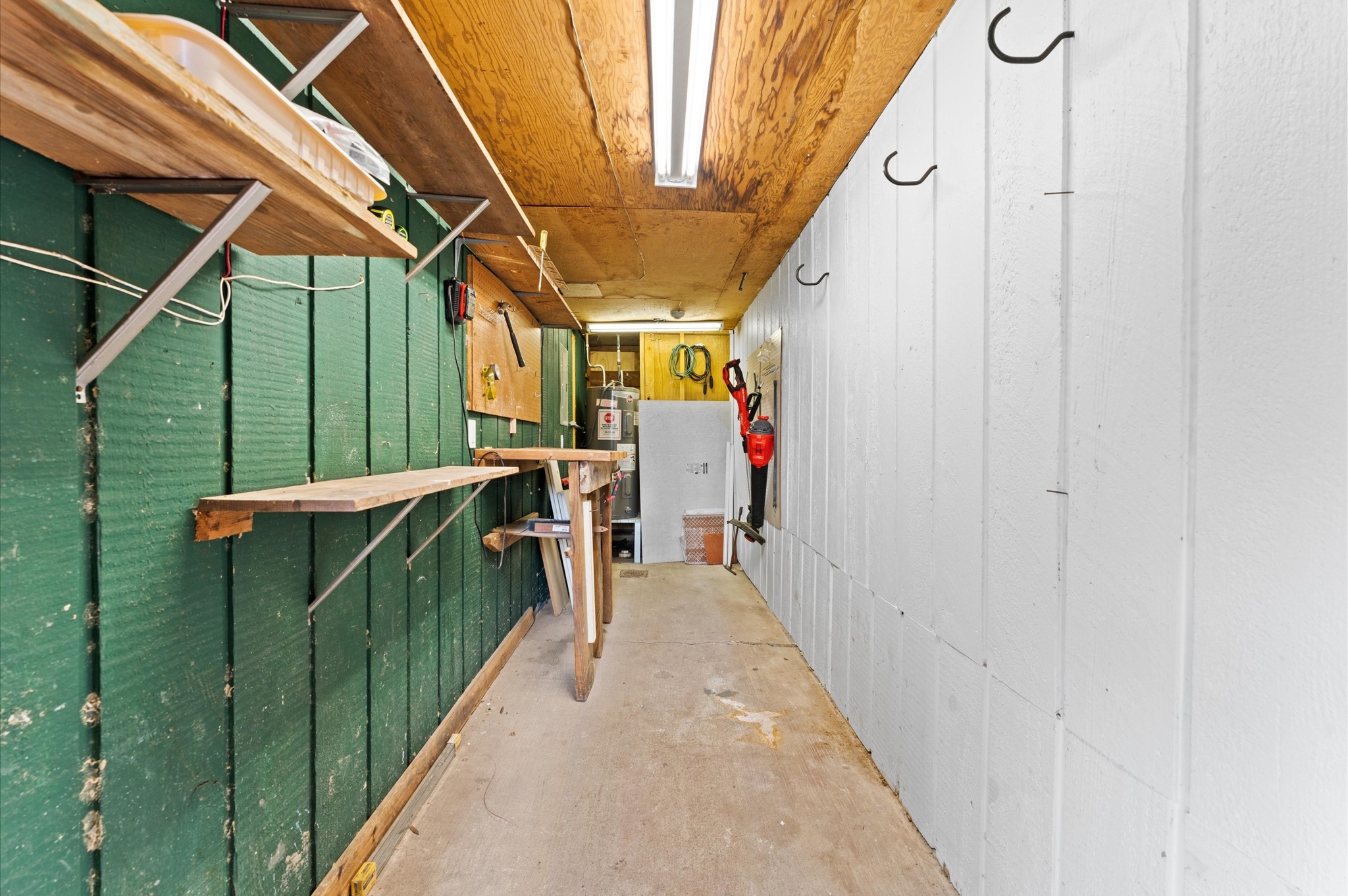 9407 Brooding Oak Circle Houston, TX 77096 - Photo 36 of 43 Storage room with wooden shelves, hooks for hanging items, and a workbench. Perfect to store your lawnmower!