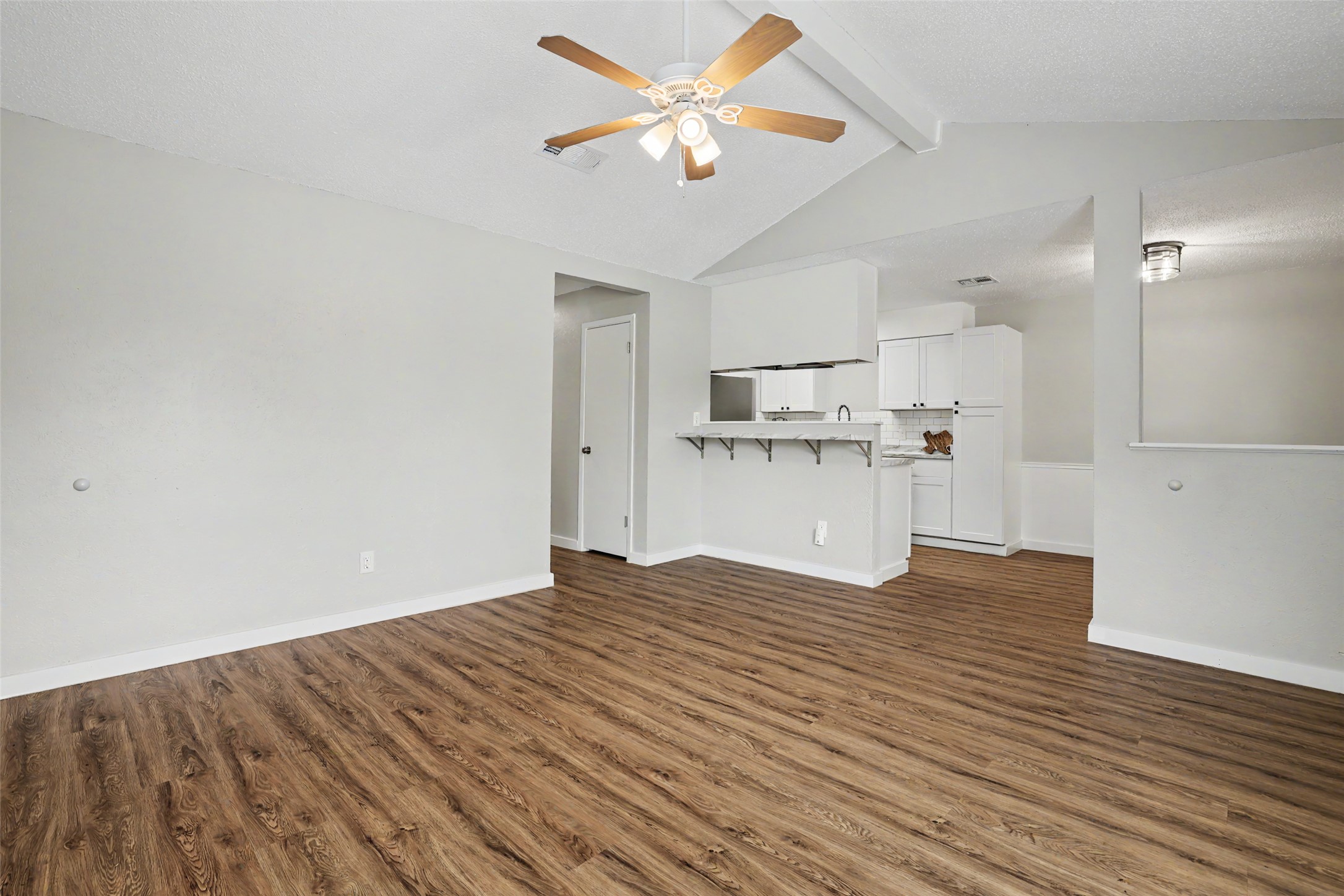 A living space offers seamless flow into the kitchen, featuring vaulted ceilings and durable wood flooring.