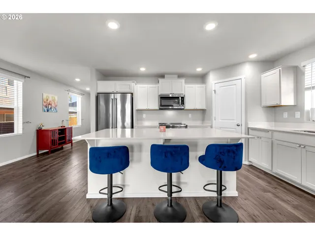 a kitchen with stainless steel appliances kitchen island granite countertop a refrigerator a stove a sink dishwasher with a dining table and chairs with wooden floor