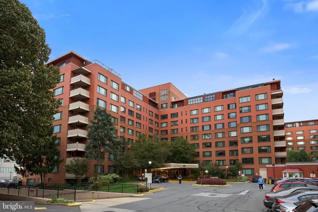 a front view of a building with lot of cars and trees