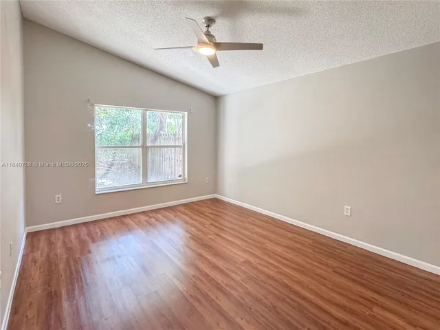 an empty room with wooden floor ceiling fan and windows