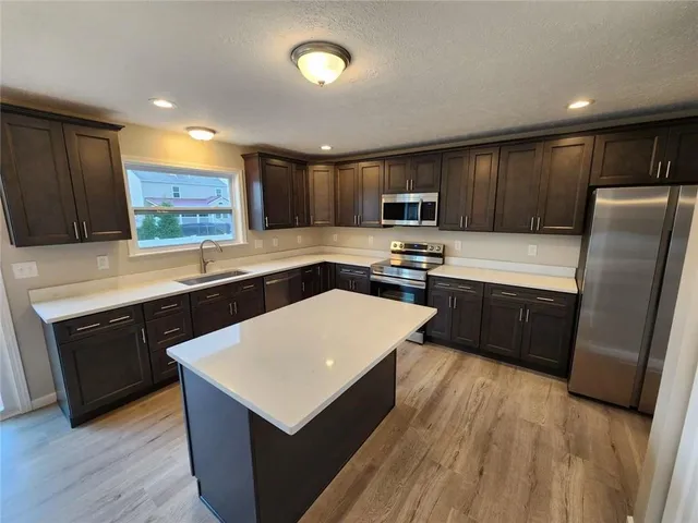 a kitchen with stainless steel appliances a refrigerator a sink a stove a microwave a center island and wooden floor