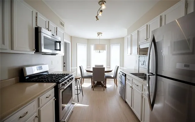 a kitchen with stainless steel appliances a stove a sink dishwasher a refrigerator white cabinets and wooden floor