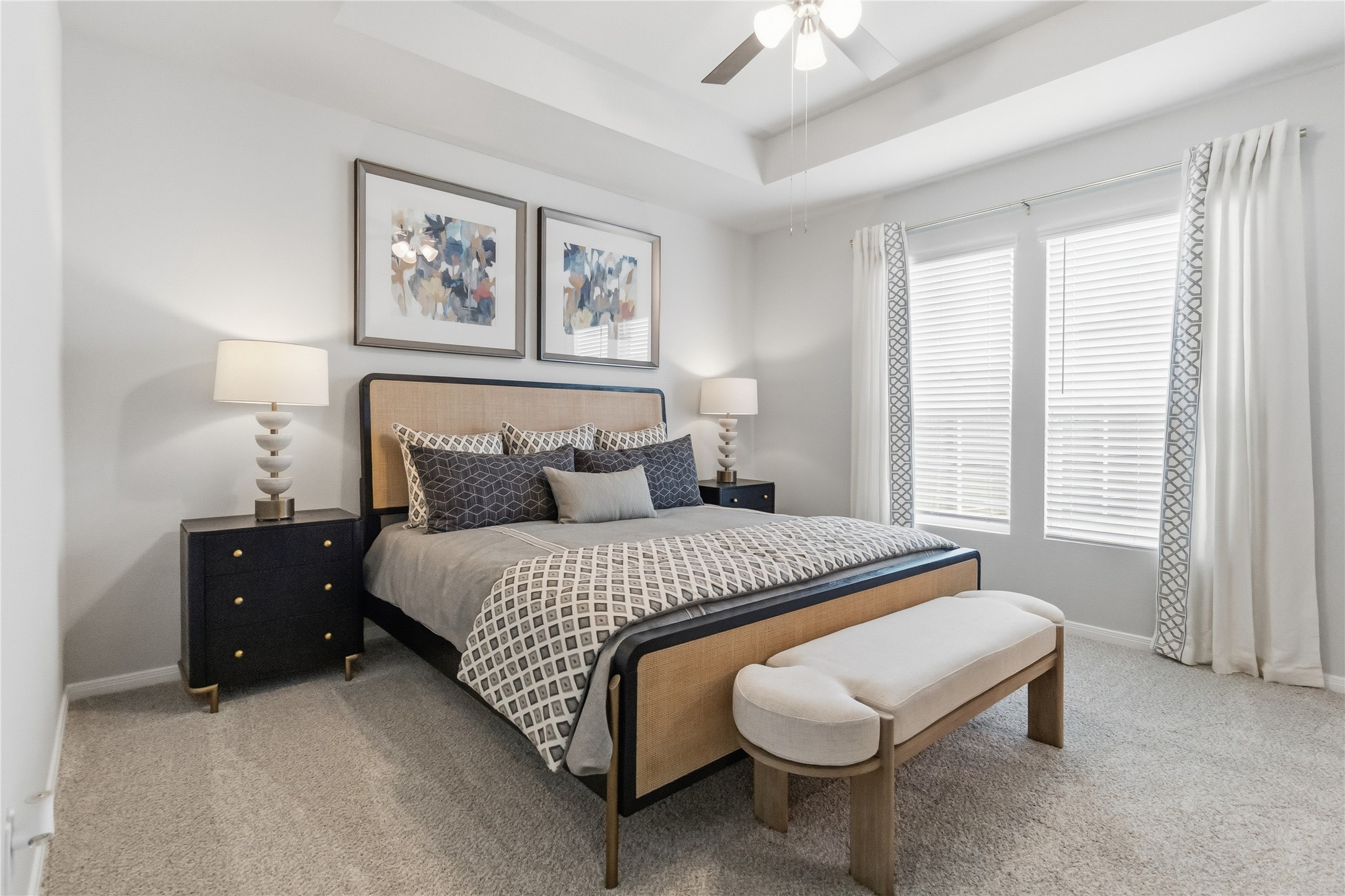 Plentiful natural light streams through tall windows into this serene bedroom with tray ceilings.