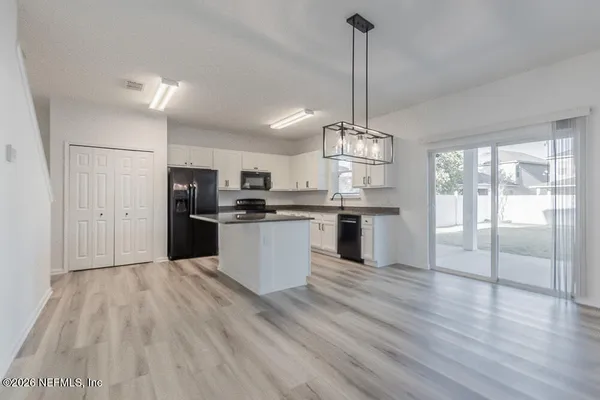 a kitchen with stainless steel appliances kitchen island granite countertop a refrigerator a sink dishwasher a stove and white cabinets with wooden floor