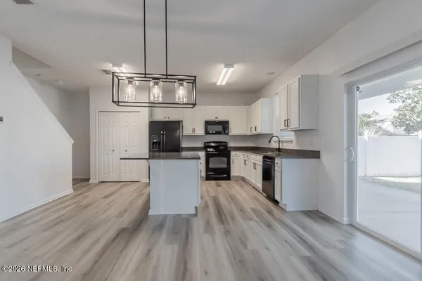 a kitchen with stainless steel appliances kitchen island granite countertop a refrigerator a stove top oven a sink dishwasher and white cabinets with wooden floor