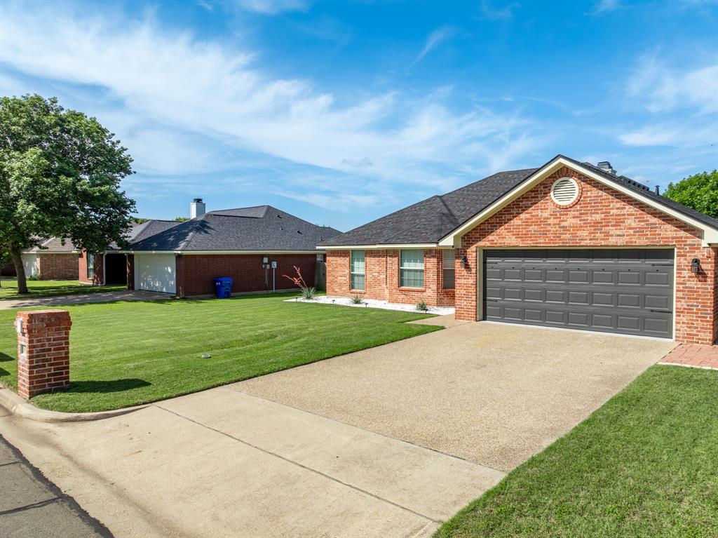 10512 Whitney Trace Drive Waco, TX 76708 - Photo 11 of 39 Brick exterior with a dark shingle roof, featuring a gray panel garage door and a decorative gable vent